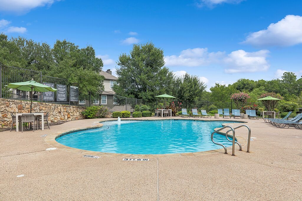 A pool surrounded by trees and chairs.